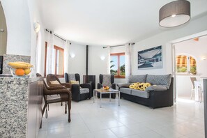En rummelig opholdsstue med sofa, stole, et sofabord og et spiseområde med bord og stole.