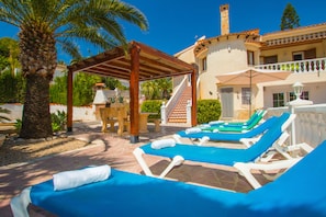 A resort with a pool area, lounge chairs, a covered seating area, and a staircase leading to a building.
