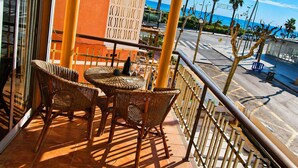 A balcony with wicker furniture, a glass door, and a view of the street and ocean. - AirCon Apartment in front of the beach (La Pineda)