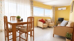A living room with a dining table, chairs, a sofa, and a television. - AirCon Apartment in front of the beach (La Pineda)