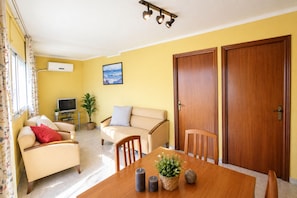 Una sala de estar con un sofá, sillones, una mesa de comedor con velas, un televisor y una planta en maceta.