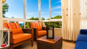 A room with a large window, wicker furniture, and a view of the sea. - VILLA BUDA  (Salou)