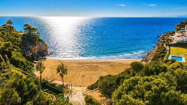 A coastal beach with a clear view of the sea, a sandy beach, and a pool area surrounded by greenery. - VILLA BUDA  (Salou)