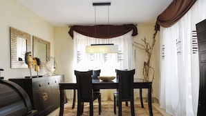 A dining area with a dark wooden table, four chairs, a chandelier, and a decorative mirror on the wall. - VILLA BUDA  (Salou)