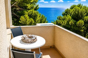 A balcony with a round table and chairs, overlooking a coastal view with trees and the sea. - VILLA BUDA  (Salou)