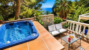 A hot tub with a stone wall, two chairs, a glass table, and a view of the ocean. - VILLA BUDA  (Salou)
