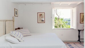 Un dormitorio con cama, almohadas, una ventana con vistas y un cuadro en la pared.