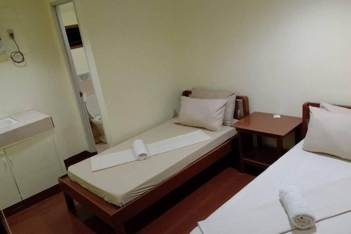 A small, single-bed room with a wooden bed frame, a small bedside table, and a mirror on the wall.