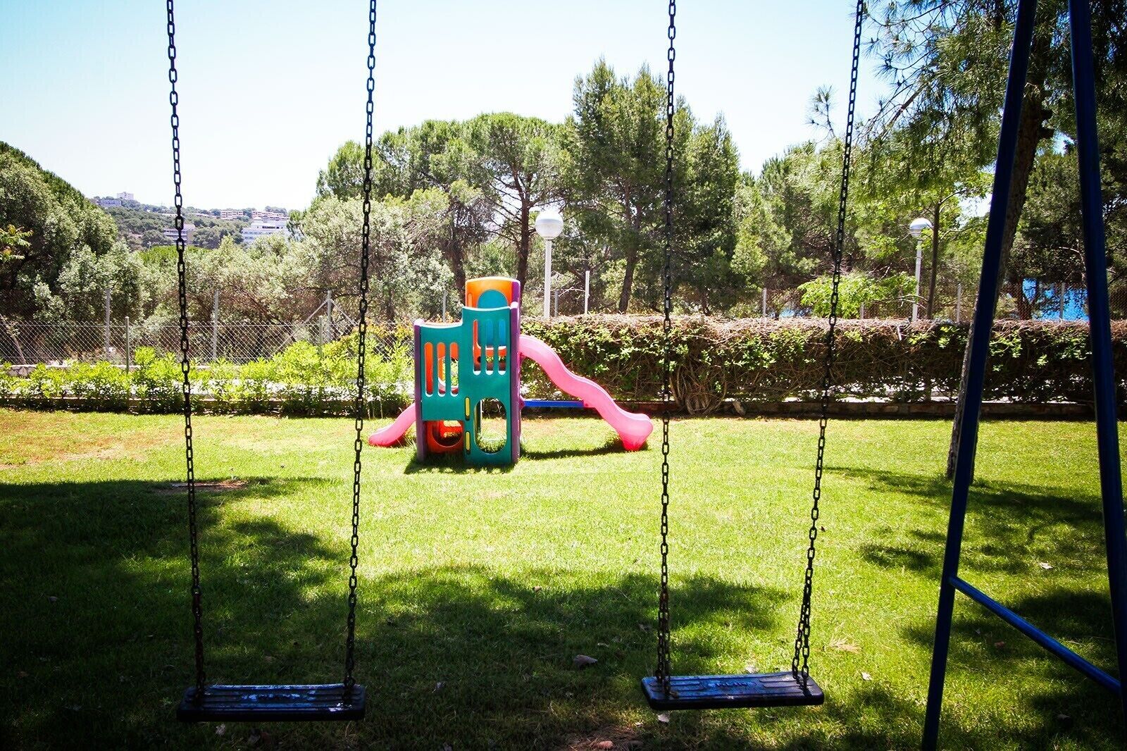 A playground with swings and a slide, surrounded by grass and trees.