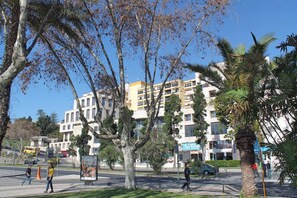 A multi-story building with balconies, surrounded by trees and palm trees.