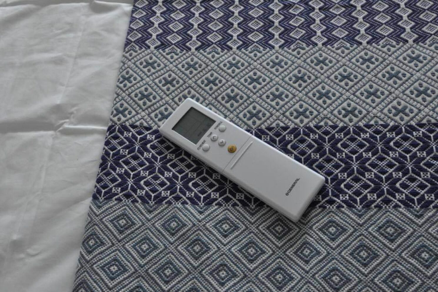 Een witte afstandsbediening op een bed met een decoratief sprei.