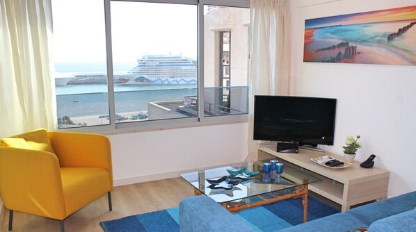 A modern living room with a large window, a television, a sofa, and a glass coffee table. - Overlooking the Marina | Petronella Marina Apt (Funchal)
