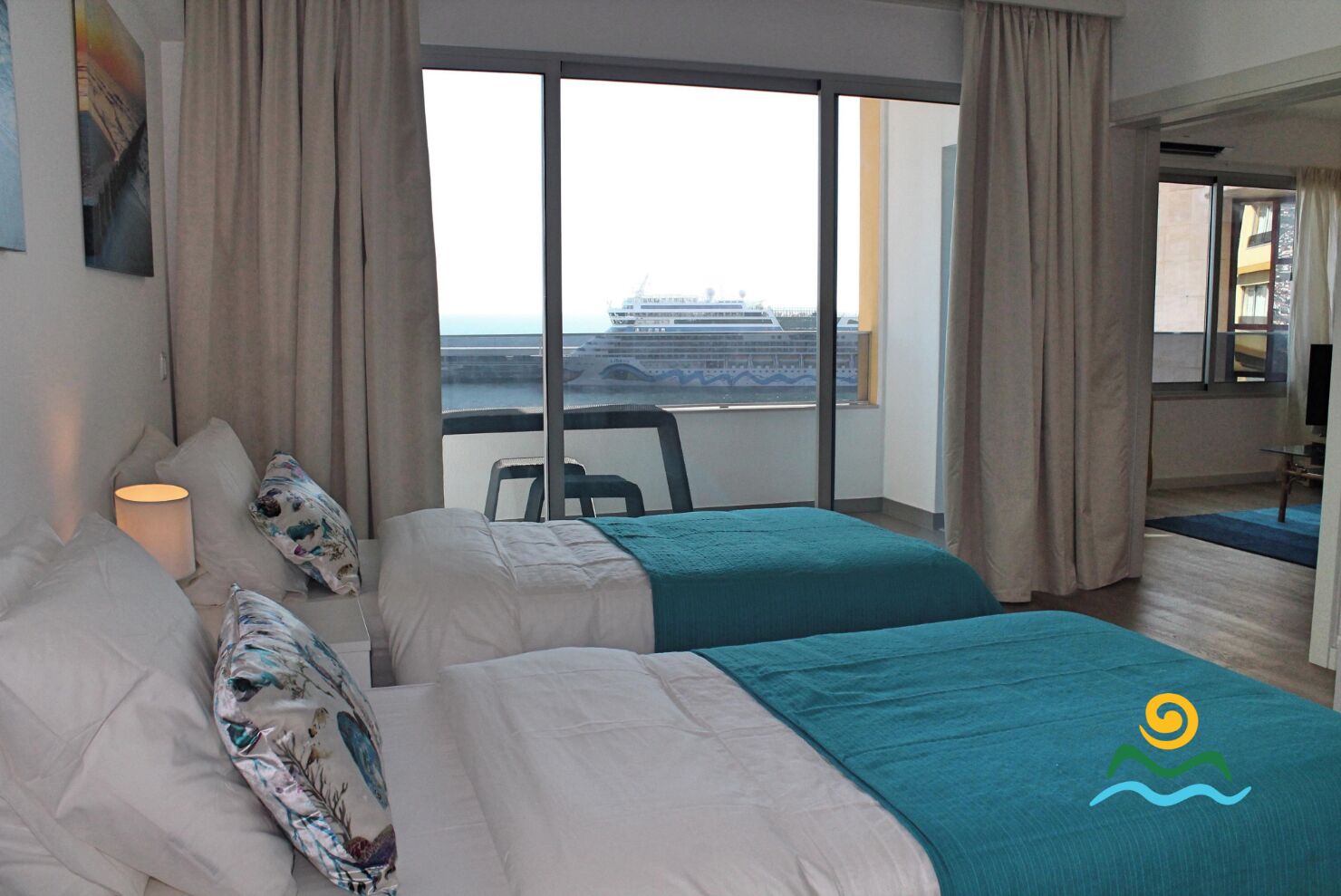 A hotel room with two beds, a view of a cruise ship, and a balcony.