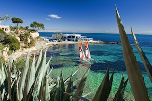 Ein Hotel an der Küste mit klarem Wasser, Palmen und einem Segelboot.