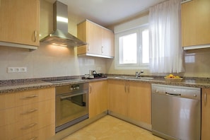 Eine Küche mit Holzausstattung, Edelstahlgeräten, einem Fenster mit Vorhängen und einer Arbeitsplatte mit Obstkorb.