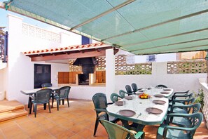 Terrassa exterior amb taula de dinar per a sis persones, amb cadires al voltant i una barbacoa de fons.