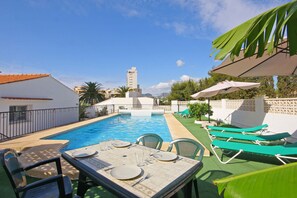 Piscina amb taula i cadires preparades per dinar, envoltada de vegetació i un cel serè.