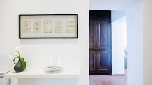 A framed artwork on a white wall, a vase with a single flower, and a white table with a plate and a candle. - Rome, Trastevere, charming apartment for 4 (Rome)