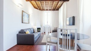 A living room with a sofa, a dining table with chairs, a TV mounted on the wall, and a fireplace. - Rome, Trastevere, charming apartment for 4 (Rome)