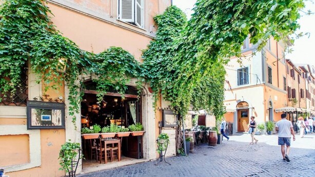 A cobblestone street with a restaurant featuring outdoor seating and greenery. - Rome, Trastevere, charming apartment for 4 (Rome)