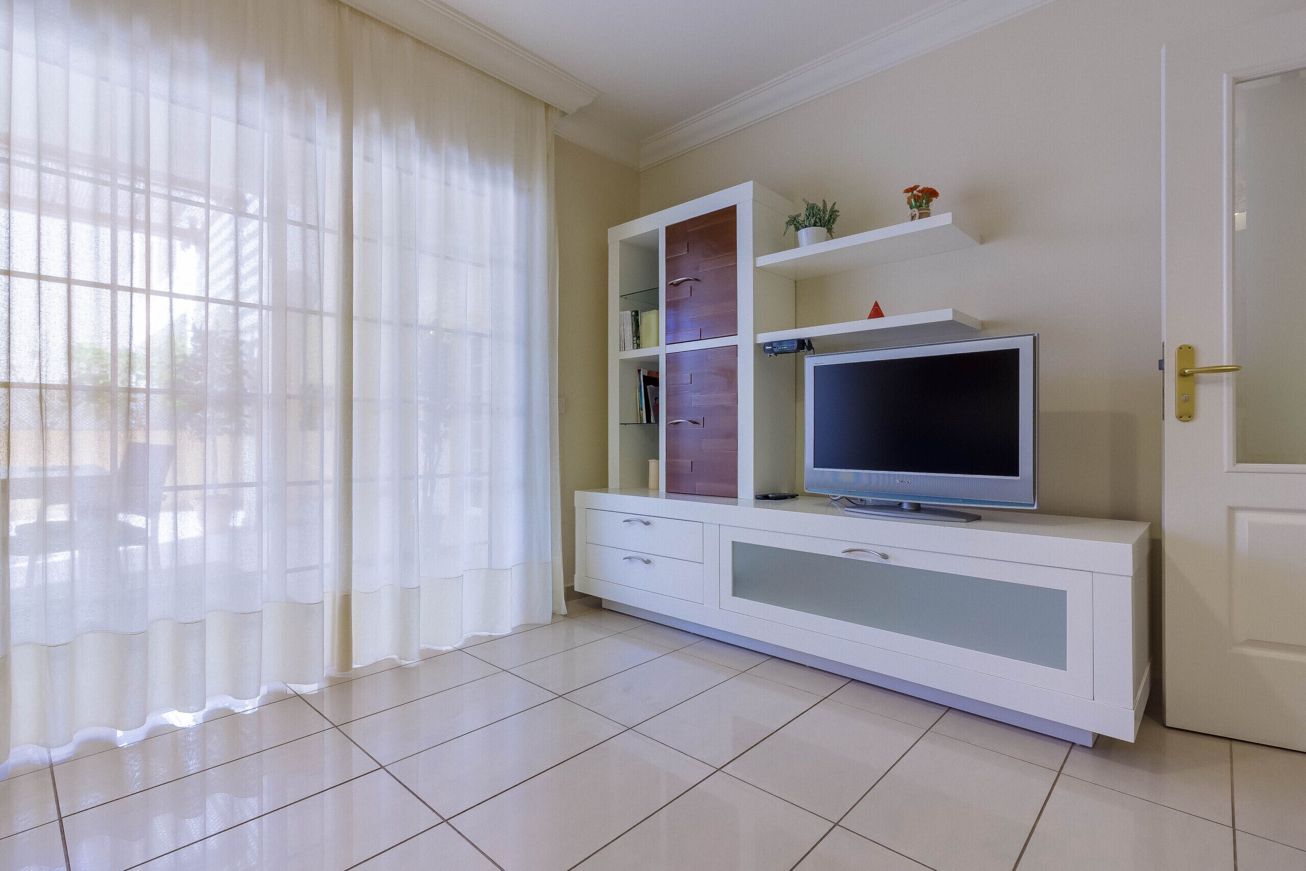 A living room with a TV on a white cabinet, a door, and a window with curtains.