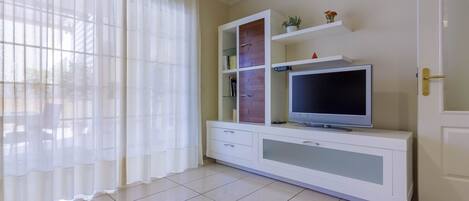 A living room with a TV on a white cabinet, a door, and a window with curtains.