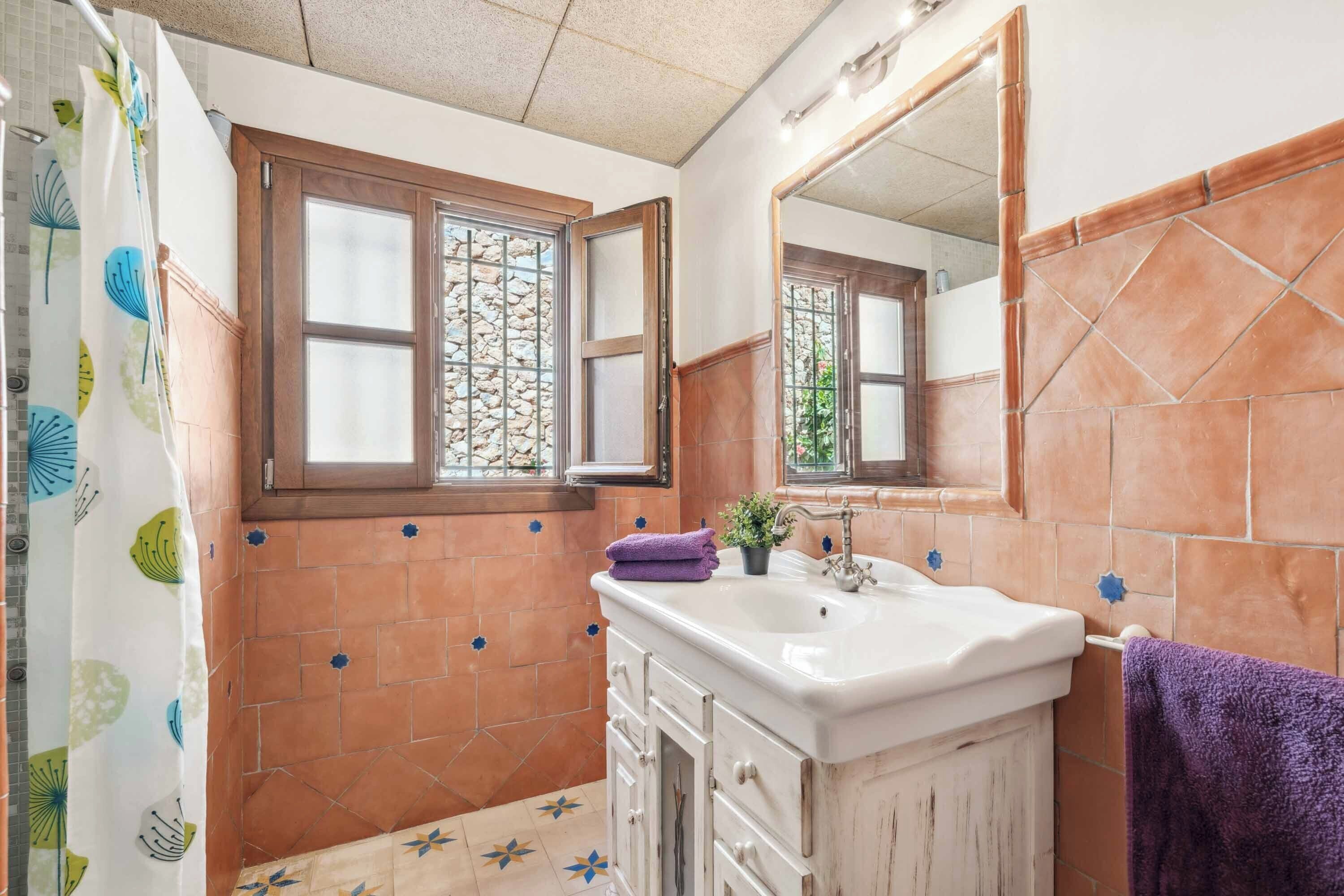 Een badkamer met een wit wastafelmeubel, een spiegel en een raam met een stenen patroon.