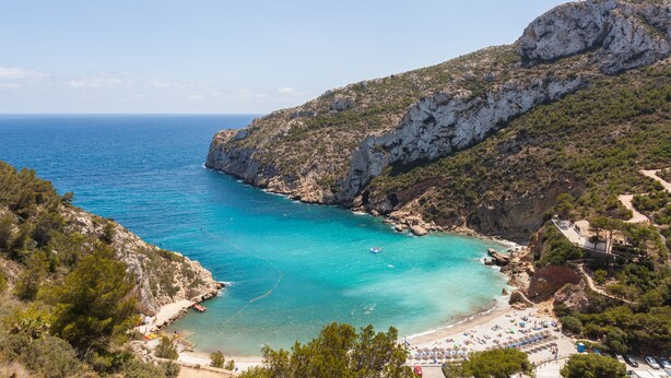 Un paysage côtier avec une plage, des falaises rocheuses et une eau d’un bleu limpide.