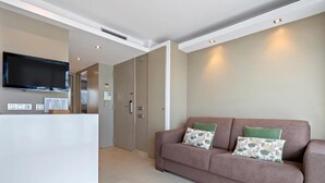 Un salon moderne comprenant un canapé, un téléviseur à écran plat, un comptoir d’accueil et une porte donnant sur une autre pièce.