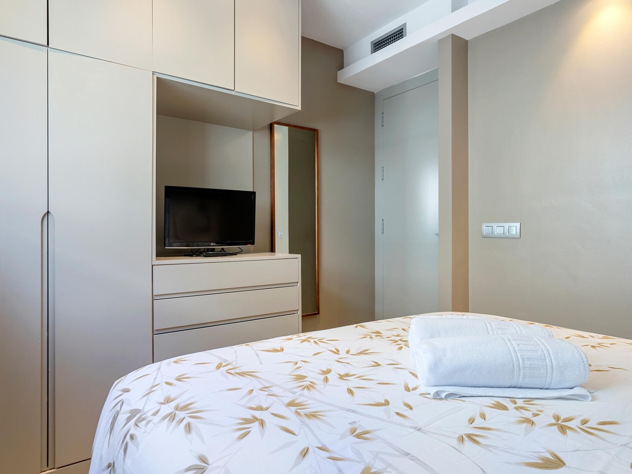 Un dormitorio con cama, televisor sobre una cómoda y armario.
