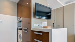 Une cuisine moderne dotée d’un four, d’un micro-ondes et d’un lave-linge encastrés, d’un téléviseur à écran plat fixé au-dessus du plan de travail et d’un design minimaliste.