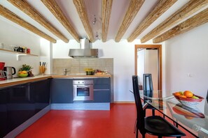 A modern kitchen with a red floor, wooden ceiling beams, and a glass dining table with chairs. - Lion's 4 (Venice)