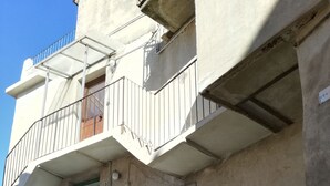 Un edificio de varios pisos con una escalera que conduce a un nivel superior. Se observa un balcón con barandilla metálica y una puerta con un número.