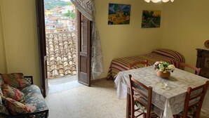 Una habitación con una mesa de comedor, sillas, un sofá, una cortina estampada y vistas a edificios a través de una ventana.