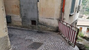 Un patio empedrado con una reja de metal, una barandilla roja y blanca, y un edificio con una puerta y un letrero que dice "VIA BELLINI".