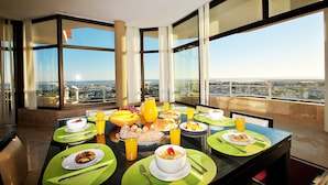 Un restaurant situé dans un hôtel de grande hauteur, offrant une vue panoramique sur la ville, et proposant un buffet de petit-déjeuner avec un choix varié de plats et de boissons.