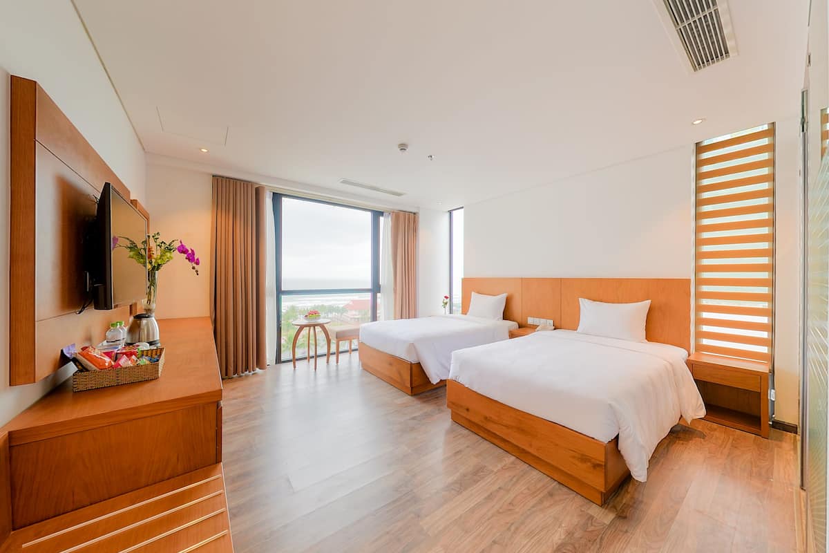 Habitación de hotel con dos camas, televisión, escritorio de madera, una mesita con un florero y un ventanal con vistas.