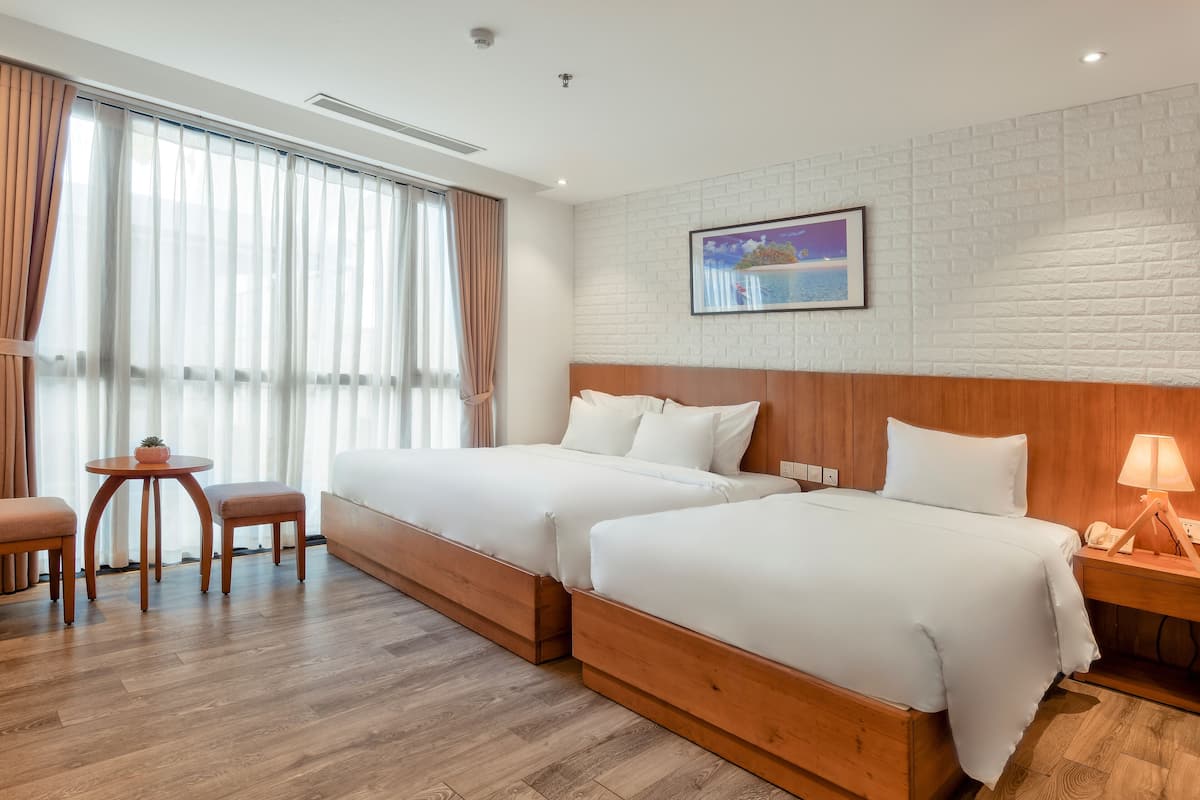 Habitación de hotel con dos camas, cabecera de madera, una mesita con una planta y una mesita de noche con lámpara.