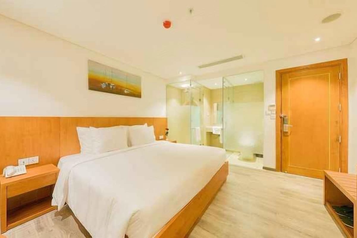 A hotel room with a large bed, a wooden headboard, a nightstand, a bedside table, and a door leading to a bathroom.