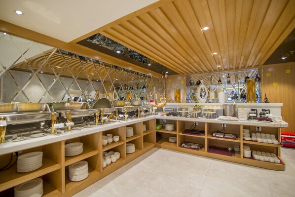 A buffet setup with multiple serving stations, shelves with plates, and a variety of food items. - Soho Boutique Hotel (Da Nang)