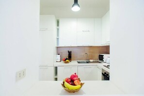 Une cuisine moderne avec des meubles blancs, un évier, un four à micro-ondes et un panier de fruits posé sur le plan de travail.