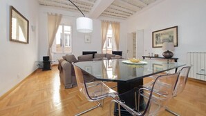 A modern living room with a glass dining table, clear chairs, a sofa, and a ceiling with exposed beams. - Rome, near Piazza di Spagna, modern and spacious apartment for 8 (Roma)