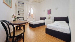 A room with two beds, a dining table, a chair, a bookshelf, and a window with curtains. - Rome, near Piazza di Spagna, modern and spacious apartment for 8 (Roma)