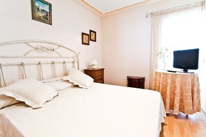 Une chambre à coucher avec un lit, une table de chevet, une lampe et un téléviseur posé sur une table près de la fenêtre.