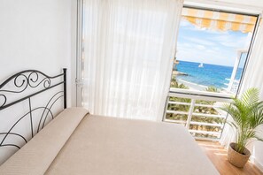 Un lit avec vue sur la mer et un voilier visible depuis le balcon.