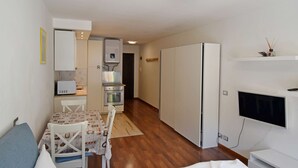 A compact living space with a kitchenette, a dining area, and a TV mounted on the wall. - EMERALD 37 STUDIO 022143-AT-672308 (Madonna di Campiglio)