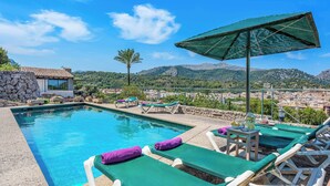 A pool area with lounge chairs, a table with drinks, and a view of a town and mountains in the background. - Ca na Copea - Four Bedroom Villa, Sleeps 7 (Pollença)