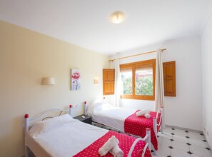 Ett hotellrum med två sängar, ett fönster med träpersienner, en tavla på väggen och ett klinkergolv.