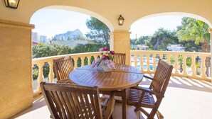 Un patio techado al aire libre con una mesa redonda de madera y sillas, un florero y vistas a un paisaje montañoso.