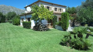 A two-story house with a well-maintained lawn, a large tree in the front yard, and a mountain in the background. - VILLA VOLANTI - 10 MIN WALK TO THE OLD TOWN (Pollensa)